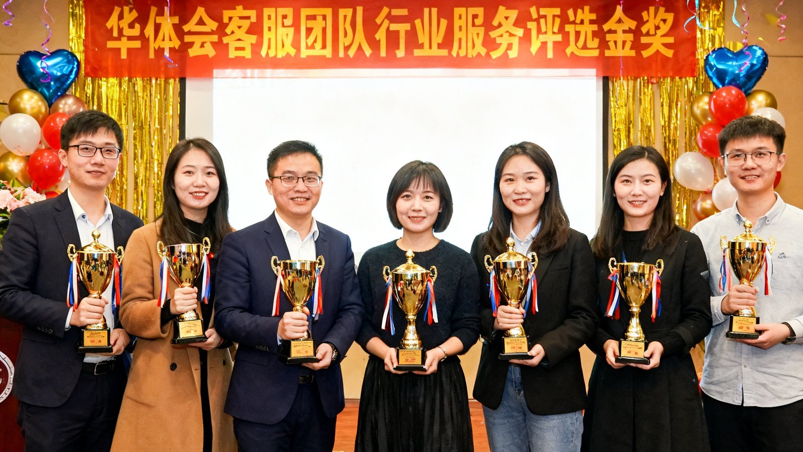 华体会客服团队在行业服务评选中荣获金奖，团队成员手持奖杯合影，背景为表彰大会现场横幅和庆祝装饰。